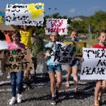 Group of people holding protest signs at an outdoor event on a sunny day, marching together.