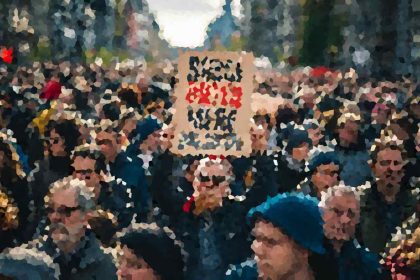 Crowd of people in a street protest, holding a large cardboard sign with red and black writing that is not legible from a distance.