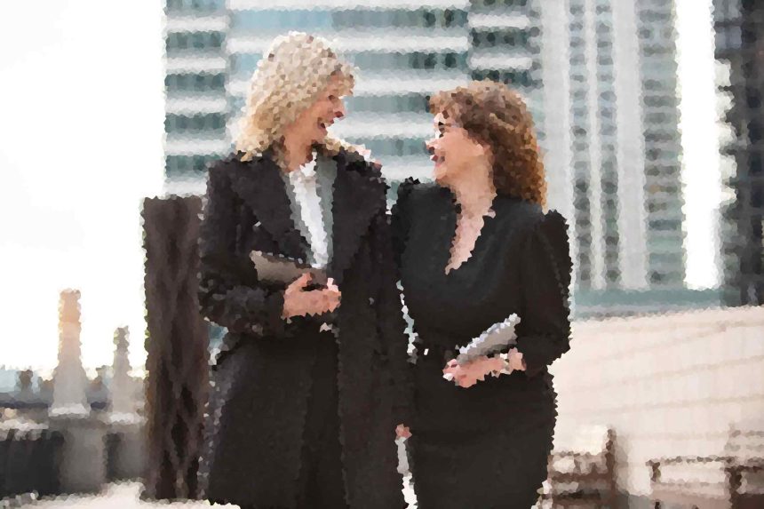 Two women in black outfits laughing and talking outside a modern glass building outside a city office.
