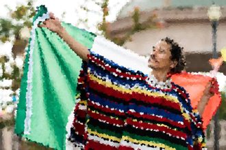 Woman outdoors, holding a large colorful striped blanket or poncho, with a green garment nearby on a clothesline or rack behind her