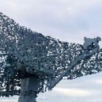 Large radio antenna (satellite dish) structure extending into a cloudy sky, viewed from the side.