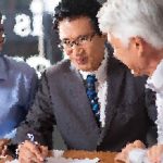 Three men in business attire leaning over a table, discussing a document together.