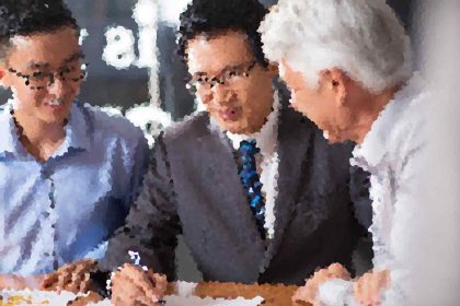 Three men in business attire leaning over a table, discussing a document together.