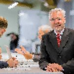 Two men in suits shake hands across a conference table during a business meeting, with colleagues talking in the background.