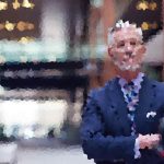 Blurry portrait of a man in a blue suit posing outdoors, smiling.