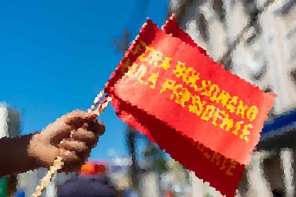 A hand holding a red protest banner with yellow text against a blue sky.