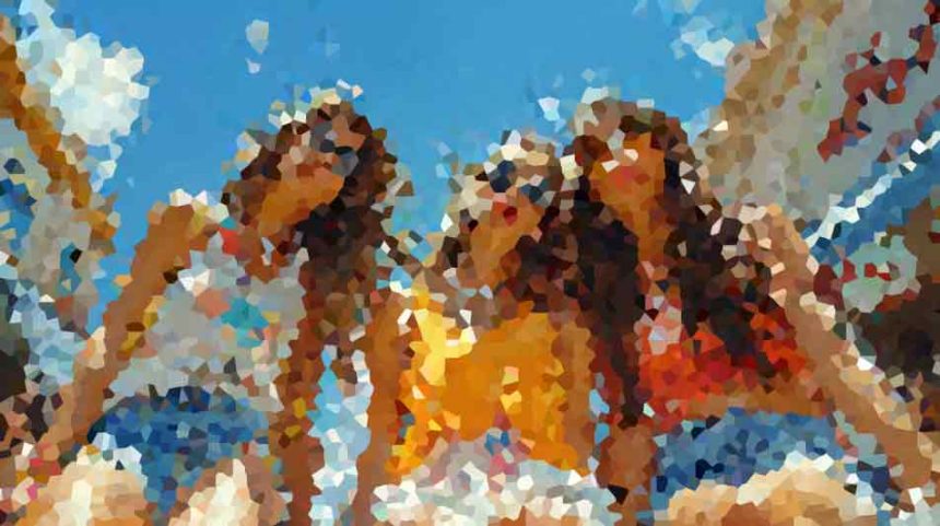 Group of people in swimsuits with arms raised, enjoying a sunny day at a water park or pool area under a blue sky.