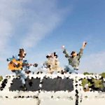 Three people celebrate on top of a white car, arms raised, on a sunny day with a rural landscape behind them.