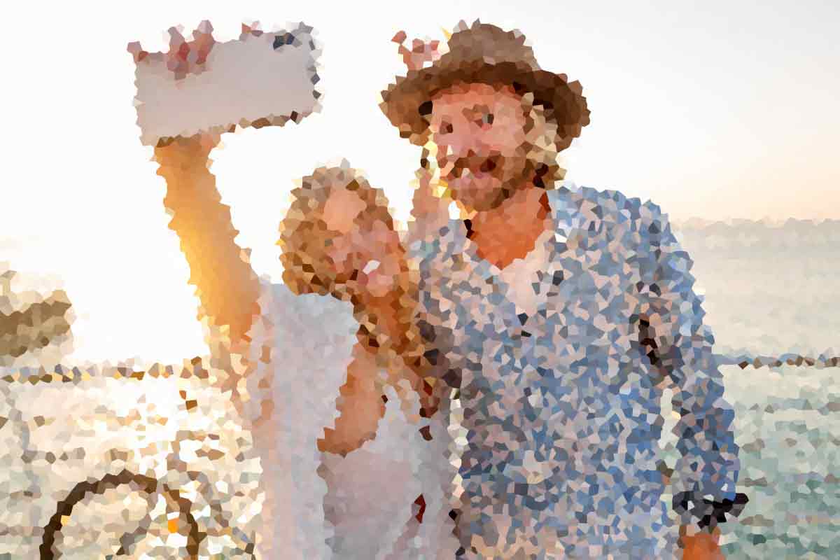 A couple on a beach at sunset, the woman in a white dress raises a sign while the man in a hat smiles beside her (stylized photo).