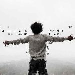 Person standing on a hilltop with arms outstretched, seen from behind in a grayscale low-poly style.