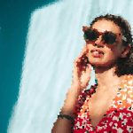 Person wearing a red floral shirt and sunglasses, talking on a cellphone against a blue background.