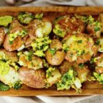Roasted baby potatoes with chopped parsley and herbs on a wooden serving board.