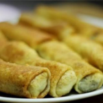Plate of golden brown fried pastry rolls arranged on a white plate, with a crispy outer crust and pale filling visible at the ends.