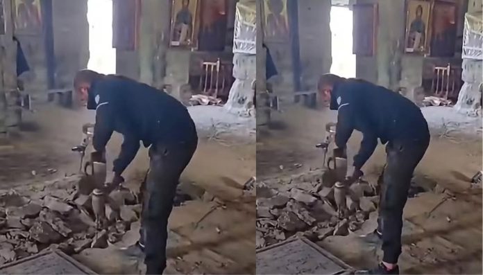 Construction worker in dark clothing chiseling rubble with a hammer inside a partially built brick room.