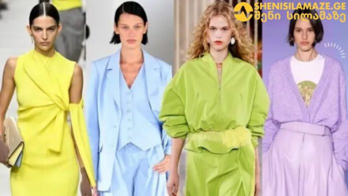 Four fashion models walk a runway in bold pastel outfits: yellow wrap dress, light blue suit, lime-green oversized ensemble, and lavender cardigan with skirt set.