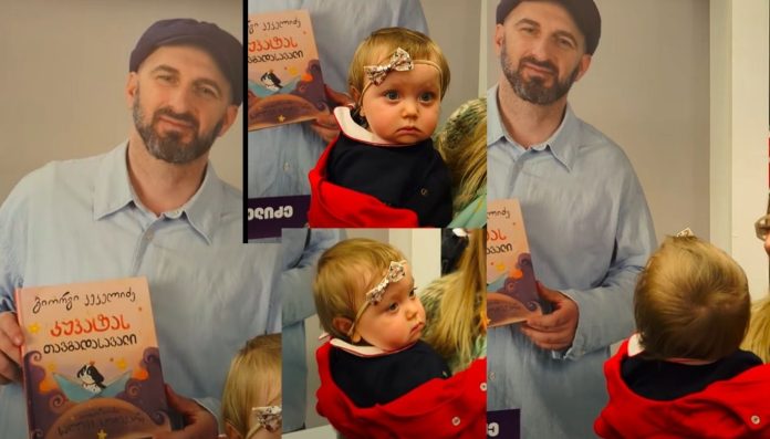 პატარა კეკე დაბნეული და გაოცებულია, ხან მამას უყურებს, ხან ბანერს - „ორი მამა გამოჩნდა“ – კეკე კეკელიძის რეაქცია წიგნის ბაზრობაზე