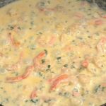 Creamy yellow sauce with diced chicken, red peppers and herbs simmering in a skillet.