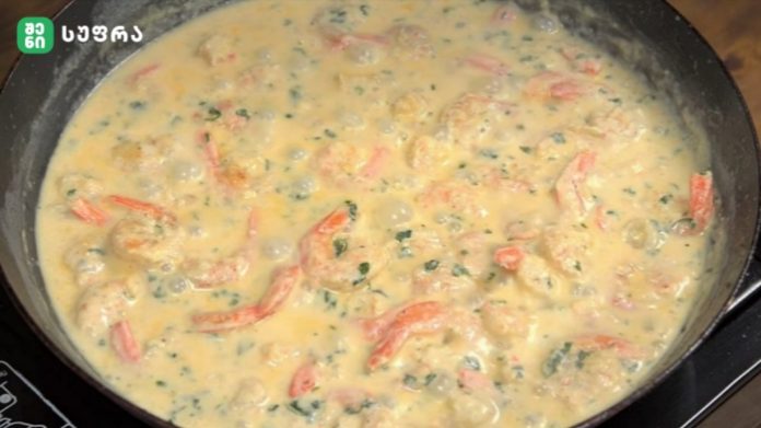 Creamy yellow sauce with diced chicken, red peppers and herbs simmering in a skillet.