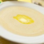 Creamy soup in a white bowl on a plate, with a small butter pat in the center.