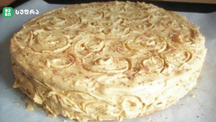 Round cake with white frosting and piped rosette decorations on top and along the sides, resting on parchment.
