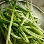 Green onions (scallions) sliced into thin spears in a metal colander, ready to rinse/or drain.
