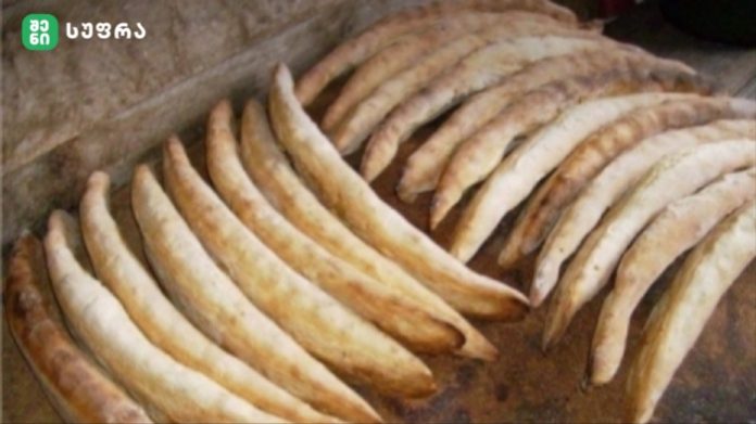 Row of curved breadsticks cooling on a baking tray, lightly browned and crusty.