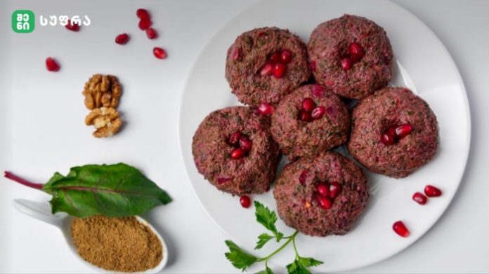 Plate of round beetroot patties topped with pomegranate seeds on a white platter with greens and spices nearby