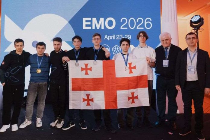 Group of young men on stage holding a Georgian flag with medals at EMO 2026 event, backdrop reads EMO 2026 April 23-29.