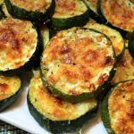 Plate of golden-brown baked zucchini rounds with melted cheese on top on a white dish.] , but remove bracket?