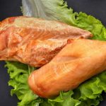 Two raw salmon fillets resting on a bed of lettuce on a dark surface.