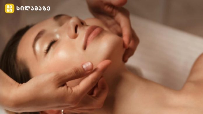 Close-up of a woman receiving a facial massage, eyes closed, as a therapist gently supports her jaw and cheekbones