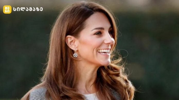 Smiling woman with long brown hair outdoors, wearing earrings, facing right side of frame with a blurred natural background.