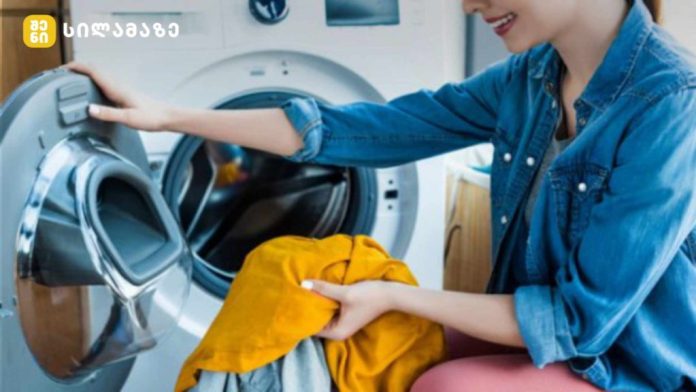 Young woman loading orange clothing into a front-loading washing machine in a laundry room.