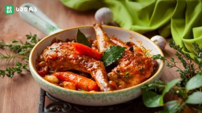 Pan of braised meat stew with carrots and herbs in a green-edged skillet on a wooden table, with a green cloth nearby.