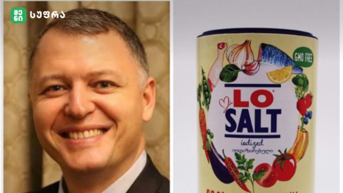 Smiling man in a suit on the left, and a colorful LO SALT iodized salt can labeled GMO free on the right.