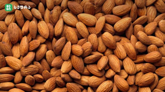 Close-up of almonds piled together, with a small green brand logo in the top-left corner.