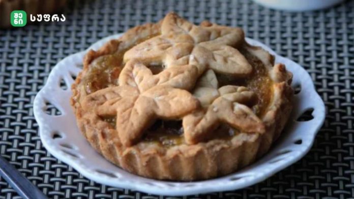 Decorative fruit tart with leaf-shaped pastry crust on a white plate, sitting on a woven table surface.