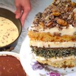 Layered cake with white frosting and chopped nuts on top, next to bowls of batter and sauce being prepared.