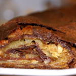Close-up of a nut-filled pastry slice with a flaky, chocolate-dusted crust on a white plate