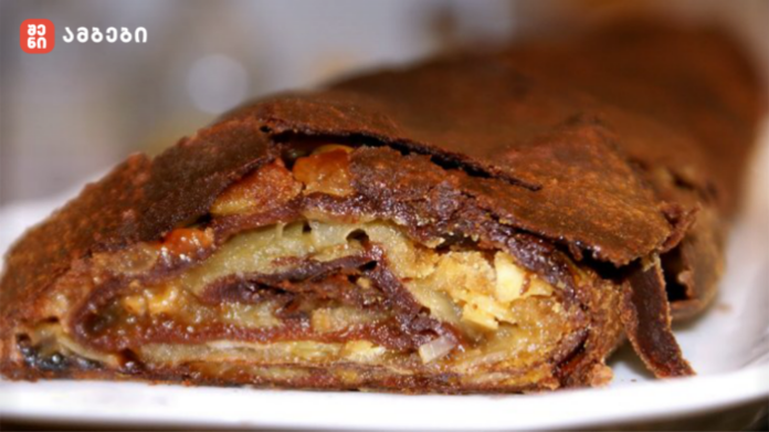 Close-up of a nut-filled pastry slice with a flaky, chocolate-dusted crust on a white plate