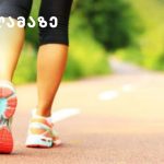 Person's legs in running shoes walking on a sunlit park path; logo appears in the top-left corner.