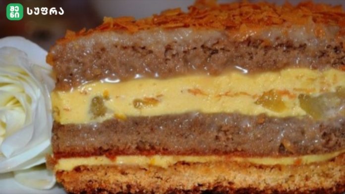 Layered cake with yellow custard filling and orange topping, displayed on a plate beside a white flower garnish.