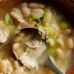 Bowl of white bean and shredded chicken soup with green onions in a wooden bowl and a spoon.