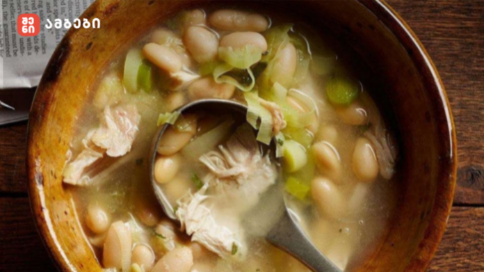 Bowl of white bean and shredded chicken soup with green onions in a wooden bowl and a spoon.