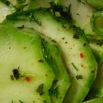Slices of cucumber with chopped dill and seasoning in a light dressing, close-up view of a cucumber salad.