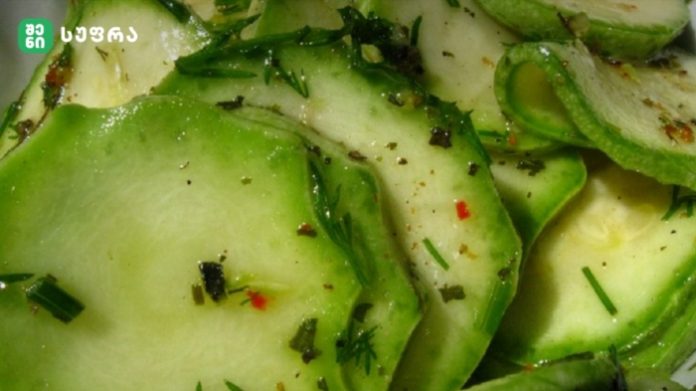 Slices of cucumber with chopped dill and seasoning in a light dressing, close-up view of a cucumber salad.