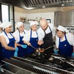 Chef demonstrates a sauce to a group of culinary students in a commercial kitchen.