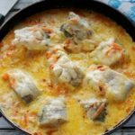 Skillet with chunks of white fish in a creamy yellow sauce with vegetables on a wooden table.