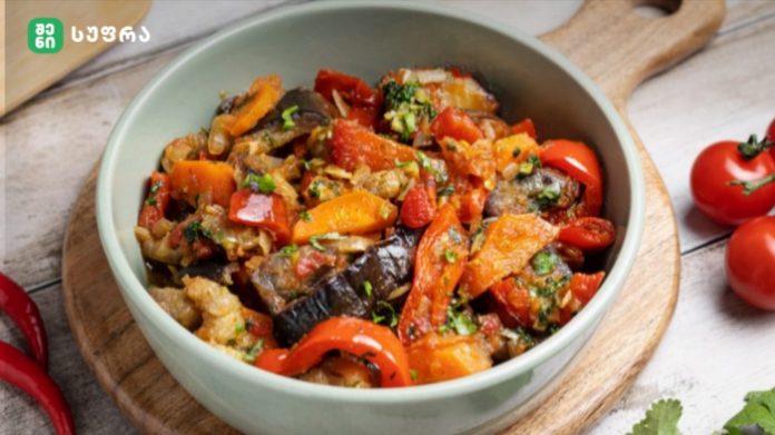 Bowl of colorful sautéed vegetables (eggplant, red and orange peppers, tomatoes) garnished with herbs on a wooden board.