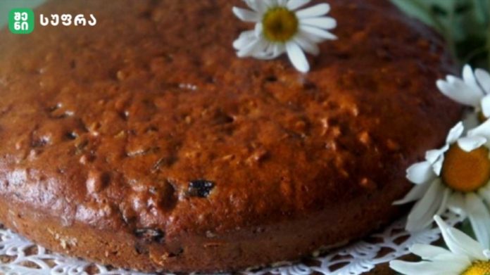 Close-up of a round golden-brown cake on a lace doily, adorned with white daisies.